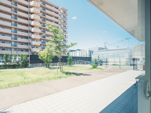 青空の下の建物と庭 敷地 静かな佇まいの建物は周囲に緑があり、清々しい日々を送ることができそうです。快適な環境での仕事をお探しの方にふさわしい場所です。