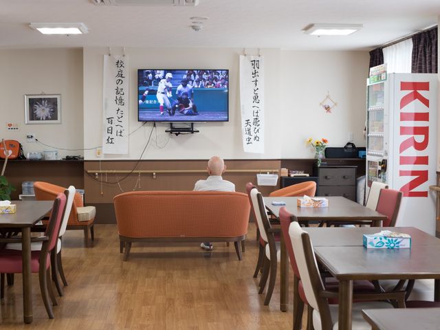 リビングで休憩する人 食堂 ゆったりとしたソファに座り、大画面のテレビでスポーツを楽しむ方の姿が印象的なリビングです。充実した共有スペースで、日々の憩いを提供します。