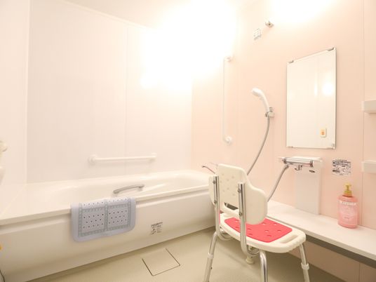 施設の写真 シャワーチェアーの前にシャンプーなどを置ける台が設置されている。浴槽の縁に滑り止めのマットが掛けられている。