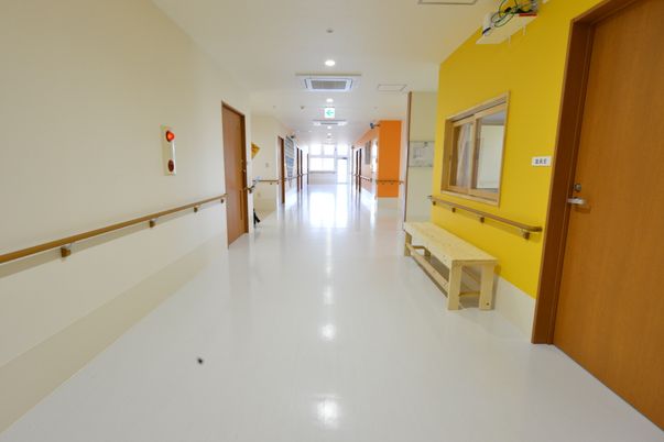 施設の写真 廊下はとても広く、片側には白いとの壁、もう片側には黄色やオレンジ色となっておりカラフルな廊下となっている。