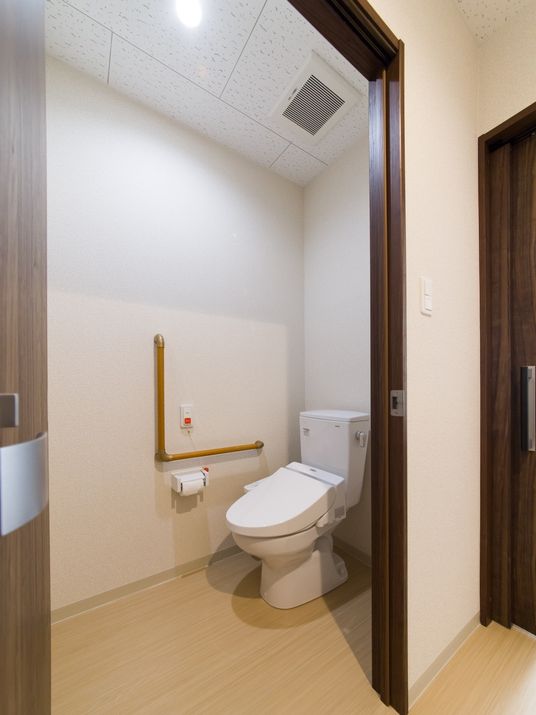 大きく開く扉に広さがあるトイレ。足元に段差は無い。壁にはＬ字型の手すりと緊急用の呼出ボタンを設置している。