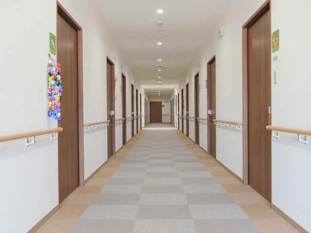 手すり付きの明るい廊下 廊下 清潔感のある廊下には手すりが設置されており、安心して歩くことができる環境が整っています。壁には明るい色の飾りがあり、温かみのある雰囲気を醸し出しています。