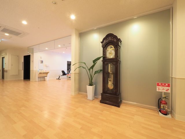 広々とした明るいロビー 廊下 ロビーには大きな時計が置かれ、落ち着いた時間が流れています。スタッフの方がデスクで業務にあたる様子も見受けられます。