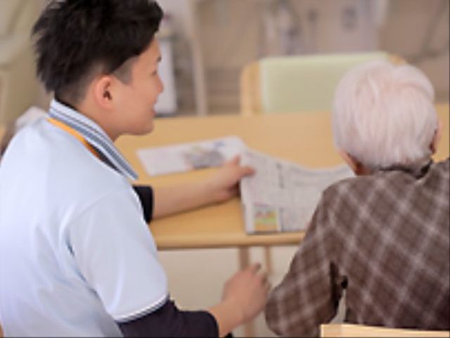 スタッフと利用者の交流 スタッフ 一緒に新聞を読む温かい雰囲気の場面です。ここでは、心を通わせる対話が大切にされています。