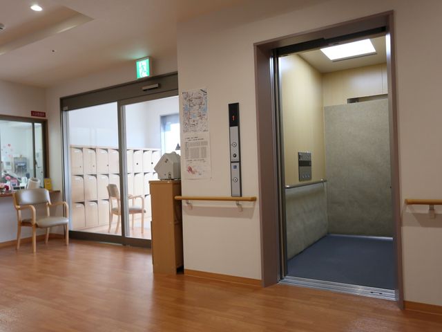 開放的なエレベーター前 エントランス ゆとりのある廊下は、足元の明るい照明により安心してお過ごしいただけます。エレベーターは手すりも完備しており、安全性に配慮された造りとなっています。