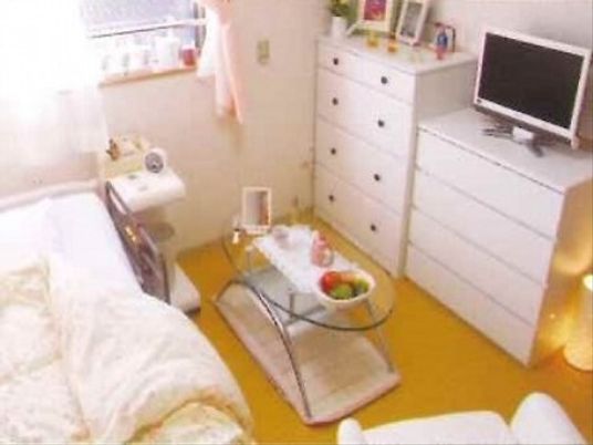 低床型のベッドの他、小型の整理ダンス２台とテレビ、１人掛けソファがある。インテリアは白で統一されている。