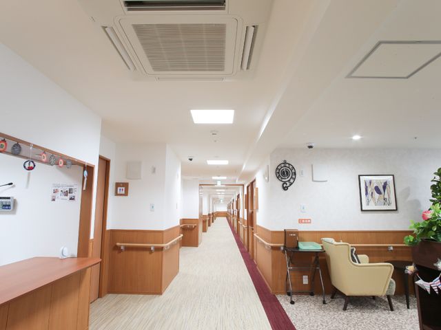 廊下の清潔な空間 通路 広々とした廊下は落ち着いた色合いで、手すりが設置され安全に配慮された設計です。温かみのある照明が心地よい雰囲気を演出しています。