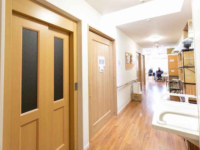 温かみのある廊下風景 廊下 木目調で落ち着いた雰囲気の廊下です。遠くにはリラックスして過ごす方々が見え、心地よい生活空間が広がっています。