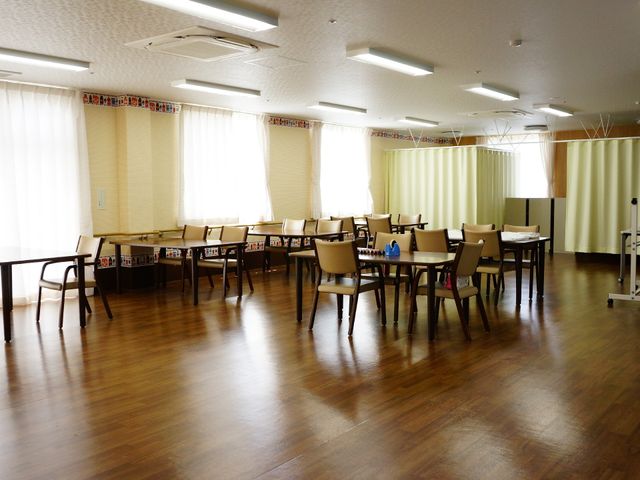 広々とした活動室 楽しく過ごせるホール 自然光が差し込む広いスペースは、様々な活動に対応可能です。ゆったりと配置されたテーブルと椅子が安らぎの時間を提供します。
