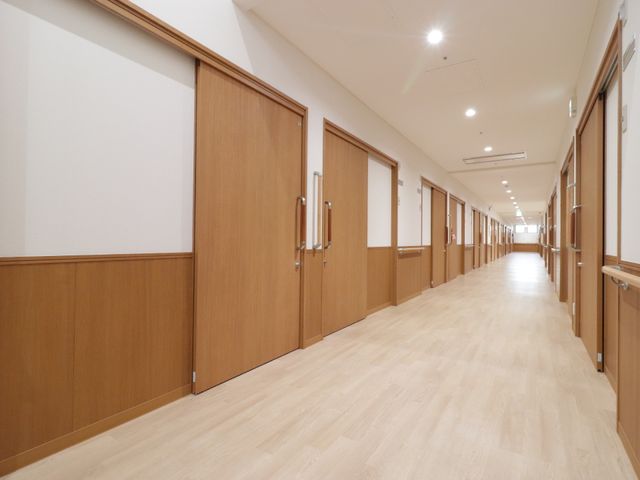 清潔感のある明るい廊下 廊下 手すりの設置された広々とした廊下は、歩行に不安のある方でも安心してご移動いただける設計です。木目調の扉が温かみを感じさせます。