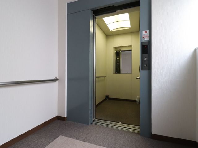廊下のエレベーター前 エレベーター 手すりが設けられた廊下は安全な移動を支えており、エレベーターもすぐ利用できる配置になっています。明るくて清潔感のある環境でのお仕事をご検討くださいませ。