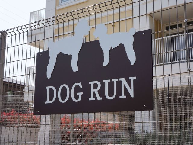 犬の形の看板があるフェンス ドッグラン ペットが自由に過ごせる空間を提供し、リラックスできる環境が整っています。快適な職場をお求めの方には、このような細やかな配慮が魅力です。