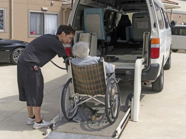 車イスの乗降支援シーン デイサービス送迎 優れた配慮で利用者様の移動をサポートするスタッフの姿です。手際よく安全に車イスを誘導しています。