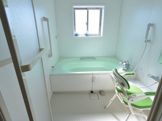 施設の写真 浴槽の外の壁や、浴槽内には手すりが付いている。また、足腰に不安のある入居者の為に、介護用のシャワー椅子が置かれている。