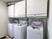 洗濯機が3台蓋が開いた状態で並んでおり、上部には乾燥機が設置されている。左側からダクトがのびている。