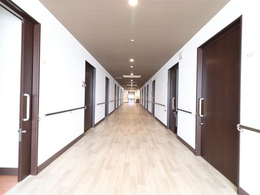 廊下の両側にはスライド式のドアが設置されており、白い壁には手すりがついており長い廊下が奥まで伸びている。