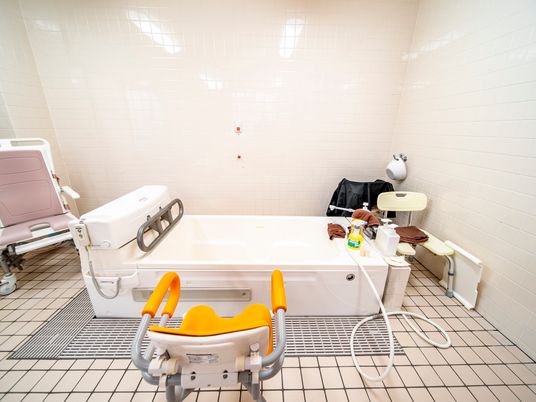 座位のままお湯に浸かることができる機械式浴槽があり、周りにシャワーチェアーが数個、使用したと思われる茶色のタオルが置かれている。