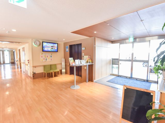 明るい廊下の一角 玄関 広々としたエントランスはゆとりある空間を提供し、ご家族との時間も心地よく過ごせます。自由に情報収集できるコーナーも備えており、来訪者を温かく迎え入れています。