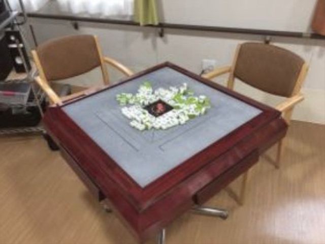 花が飾られた木製テーブル 談話スペース 落ち着いた色合いの木製テーブルが中心にあり、観葉植物で彩られた安らぎの空間です。周りにはゆったり座れる椅子も完備しております。