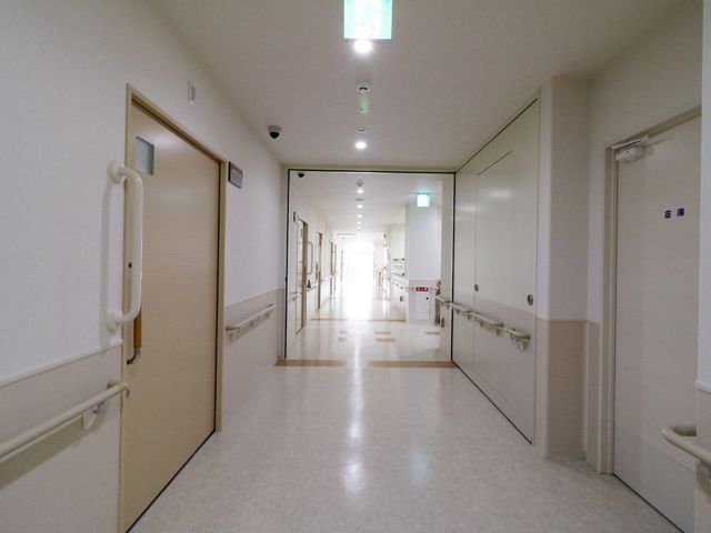 手すり付きの清潔な廊下 非常用扉のある廊下 手すりが設置され、落ち着いた色彩の廊下は安全に配慮されております。通路は広々としており、快適にお過ごしいただける空間です。