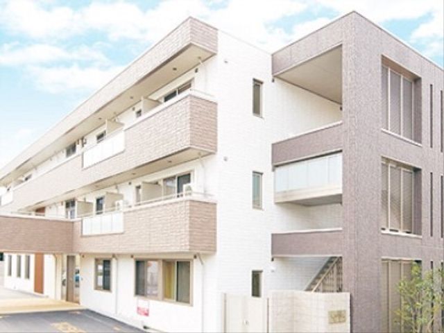 明るい日の施設外観 外観 清潔感のある白と茶色のモダンな建物です。日当たりが良好で、居心地の良い職場環境が期待できます。