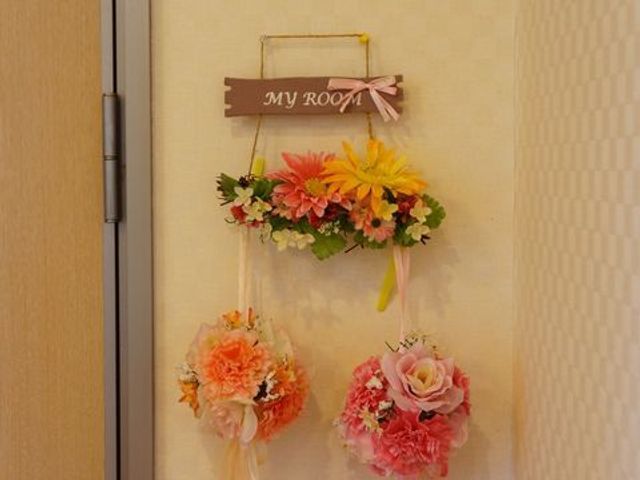 居室のドア飾り 装飾 暖かい色合いの花で彩られた居室のドアは、個々の趣向を大切にしたあたたかな雰囲気を提供しています。