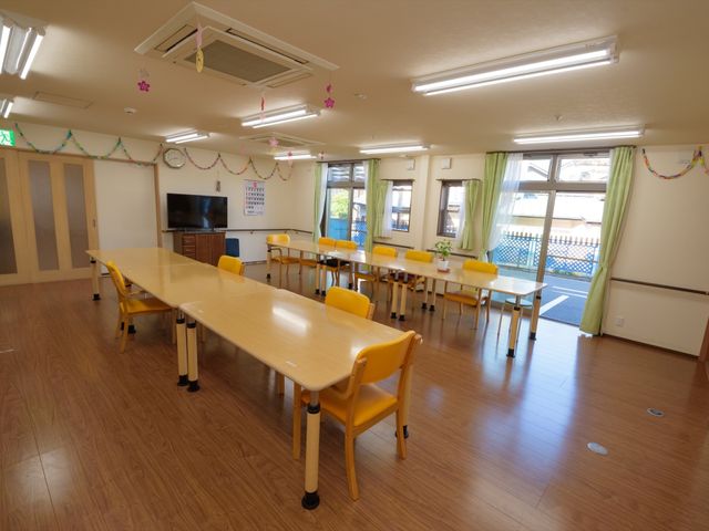 飾り付けされた明るい食堂 共有ルーム 広々とした食堂は木目調の床で温かみがあり、彩りのあるいすが並んでいます。窓から差し込む自然光で、居心地の良い空間が演出されています。