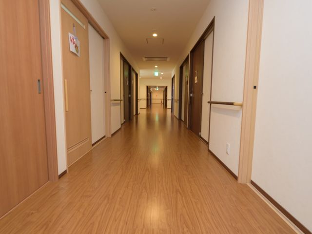 明るい廊下の様子 通路 手すり完備のゆったりとした廊下は、日々の移動が快適に行えます。壁面のデザインも落ち着いた色合いで、心安らぐ空間が広がっています。