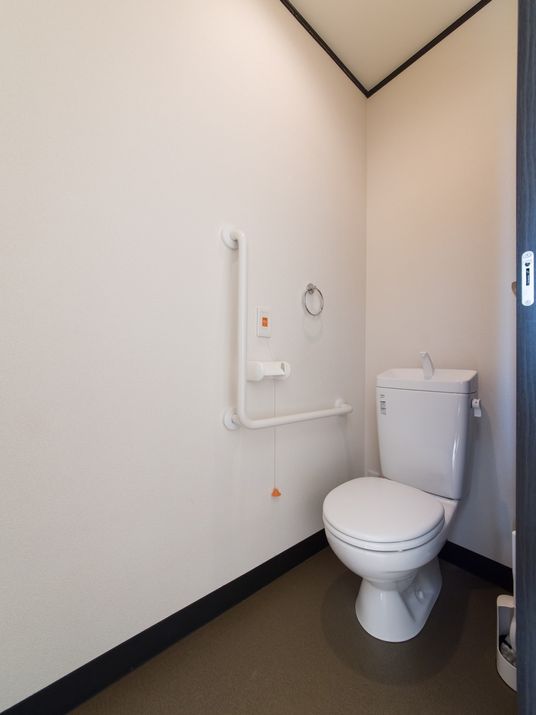 白で統一されたトイレの壁には、L字型の手すり、緊急時ボタンが取り付けられているので、安心して利用できる。