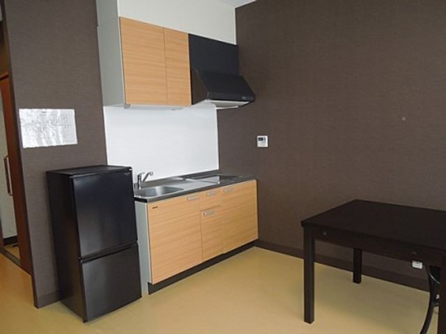 キッチン付きシンプル居室 居室 コンパクトながら機能的なキッチンが備えられた居室です。黒い冷蔵庫と木目調の収納が落ち着いた雰囲気を醸し出しています。