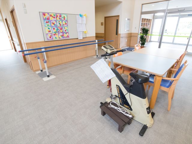 機能訓練室の広々空間 エントランス 床に敷かれたカーペットが足元の安全を支え、広々とした訓練スペースが確保されております。運動器具使用時も、しっかりとサポートいたします。