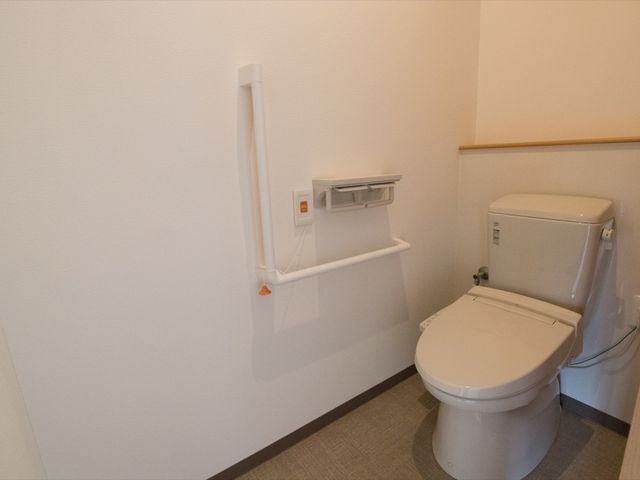 バリアフリー設計のトイレ トイレ 手すりの付いた清潔なトイレで、利用者の安全と自立を支えます。快適な日々のために細かな配慮が行き届いています。