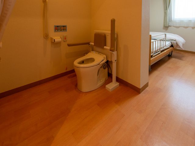 バリアフリートイレとベッド 居室 手すり付きの清潔なトイレと、窓の光が心地良いベッドスペースが整っており、快適な居住環境を提供しています。