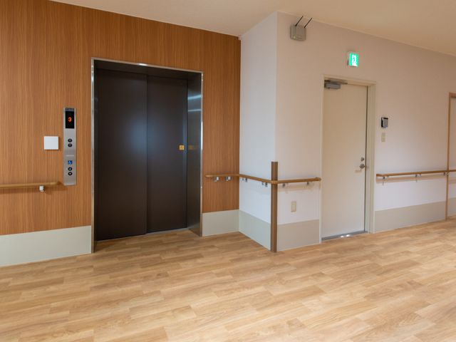 明るい廊下とエレベーター エレベーター ゆったりとした空間のエレベーター前です。壁と床の色合いが温かみを感じさせ、バリアフリー設計が実践されています。