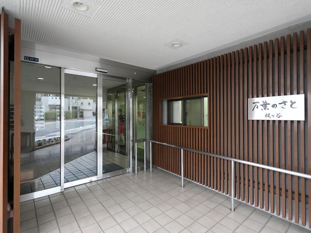 エントランスの明るい外観 玄関 ゆとりのあるエントランスは、手すり付きで安全性を考慮した設計です。職員が笑顔で迎え、あたたかな雰囲気が漂っています。