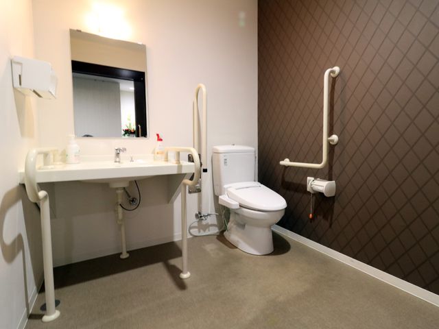 バリアフリーの洗面トイレ 多目的便所 手すり付きの洗面台とトイレを備えた清潔感のある空間です。利用者の安全と快適性に配慮した設計です。