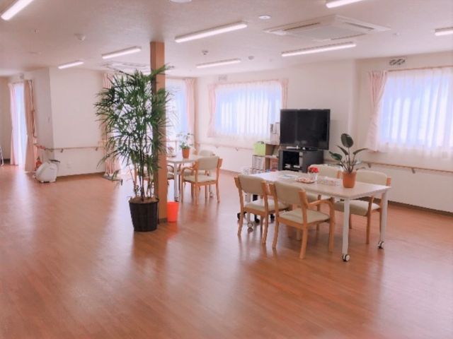 明るい共有ダイニングスペース デイルーム 広々としたダイニングルームで、ご入居者が食事やお茶を楽しんでいます。窓からの自然光が心地よい空間を創出しています。