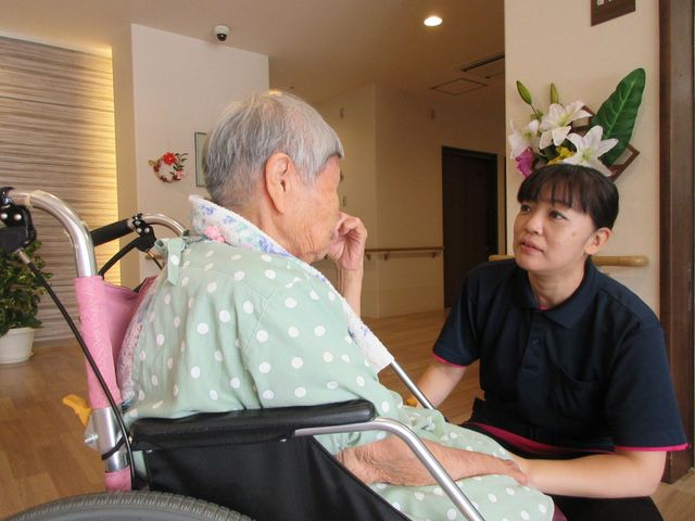 ケアスタッフと入居者の会話 居室 ケアスタッフが車椅子に座る入居者と向き合い、心温まる会話を交わしています。安心と癒しの時間を提供しています。