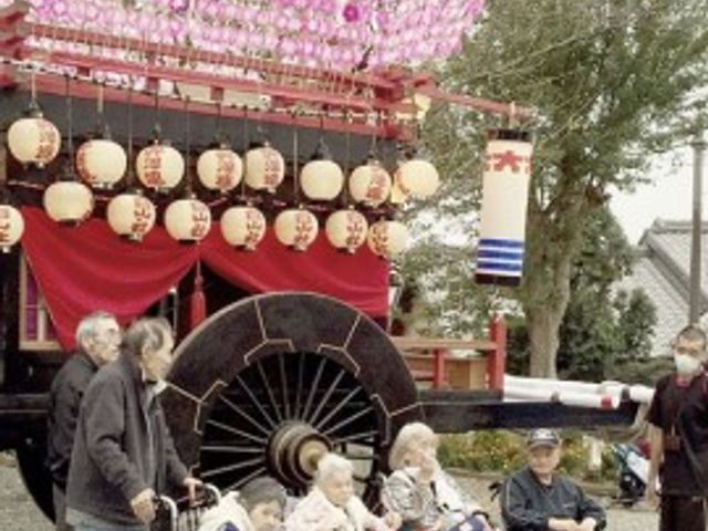祭りの屋台と利用者 レクリエーション 利用者が屋台を前に椅子や車椅子で会話を楽しむ様子です。季節ごとのイベントを通じて、心のこもった交流が育まれています。