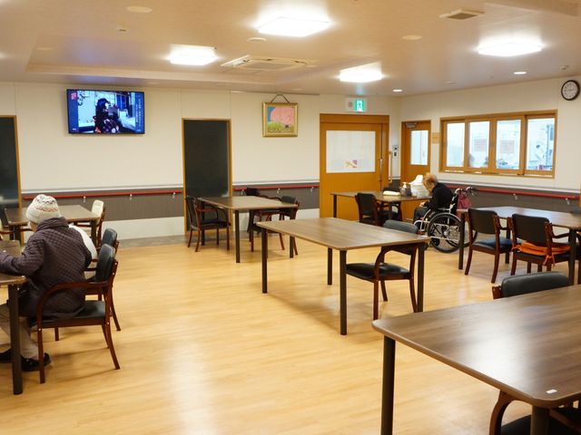 共用スペースの様子 スライドショー 広々として明るい食堂で、入居者同士のコミュニケーションが育まれる空間です。テレビを見ながらリラックスできる椅子とテーブルが配置されています。