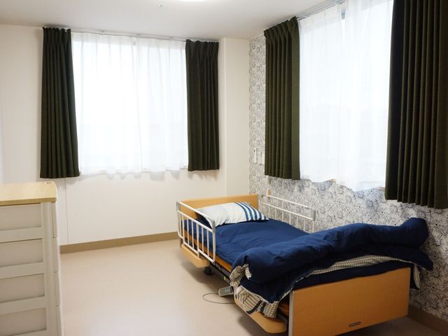 居心地の良い居室 スライドショー ゆったりとしたベッドと明るいカーテンのある居室です。必要な家具も整い、落ち着いて時間を過ごせる空間になっています。