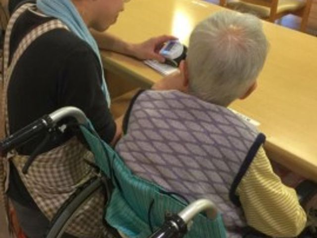 車椅子利用者とスタッフ スタッフ スタッフが優しく寄り添い、対話を楽しむ温かな雰囲気の食堂。日々のコミュニケーションが充実しており、安心してお過ごしいただける環境です。