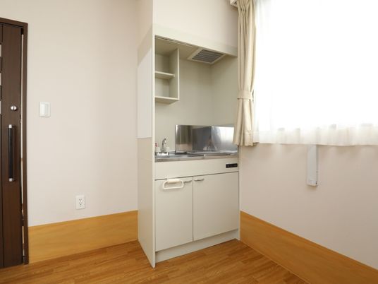 施設の写真 居室内には、ミニキッチンが備えられている。シンクの上部には棚が２段あるので収納に利用でき、隣には冷蔵庫を置くスペースもある。