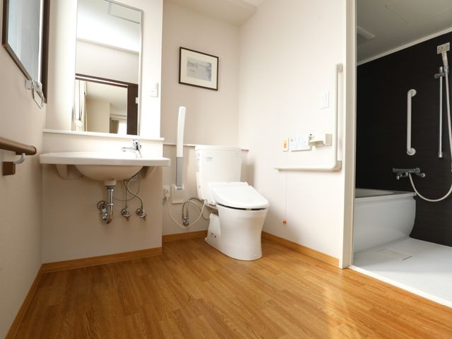 バリアフリー対応の洗面台とトイレ トイレ 手すり付きで安全に配慮された清潔感のあるトイレスペースです。ゆったりとした造りは快適な使用感を提供します。
