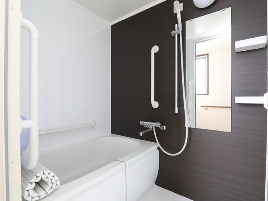 白とブラウンが基調になっており、高級感がある浴室になっている。鏡が大きく、壁には手すりが付いている。