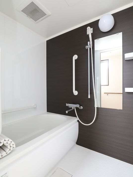 施設の写真 明るい浴室の浴槽側の壁には横方向に手すりが設置されており、入居者様はそれを使用し安全に入浴することができる。