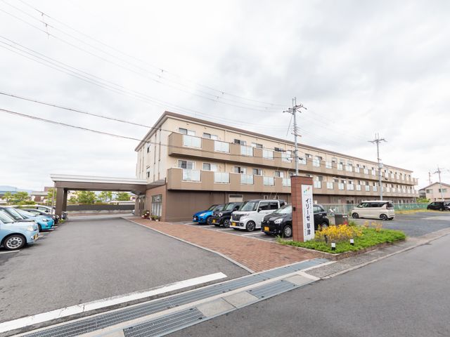 明るい外観の施設入口 外観 広々とした駐車場があり、入り口も広くて明るい雰囲気の建物です。来訪者の方々を迎えるためのきれいに手入れされた植栽もあります。