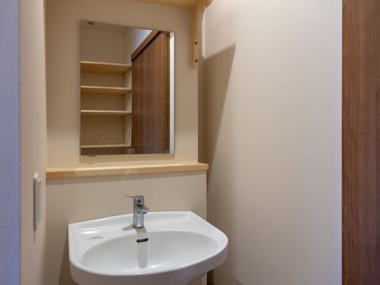 居室の一角に備え付けられたシンプルな鏡付きの洗面台は、蛇口がレバー式で使いやすい。向かい側には収納棚が見える。