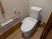 サムネイル 便器の横に操作パネルが設置されている。壁には２連のトイレットペーパーホルダーや手すり、紐付きの呼び出しボタンが設置されている。