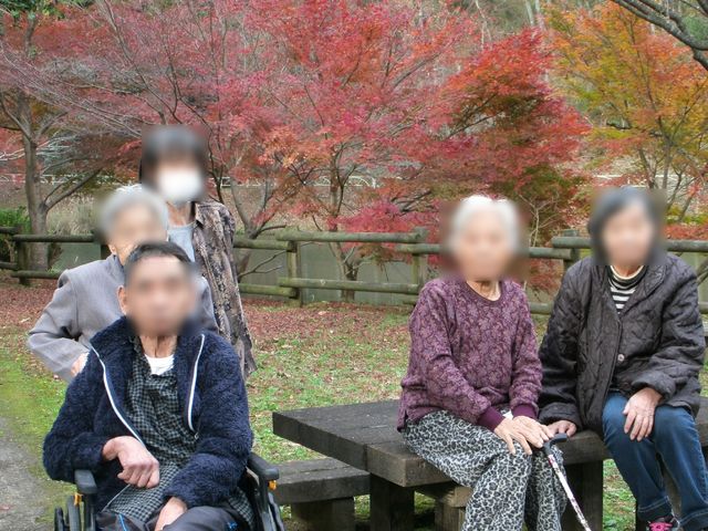紅葉を背にする休憩中の人々 紅葉狩り 季節の移ろいを感じる中庭で、穏やかな時を過ごす利用者の姿が印象的です。四季折々の自然を身近に感じられる環境で働くやりがいを感じていただけるでしょう。